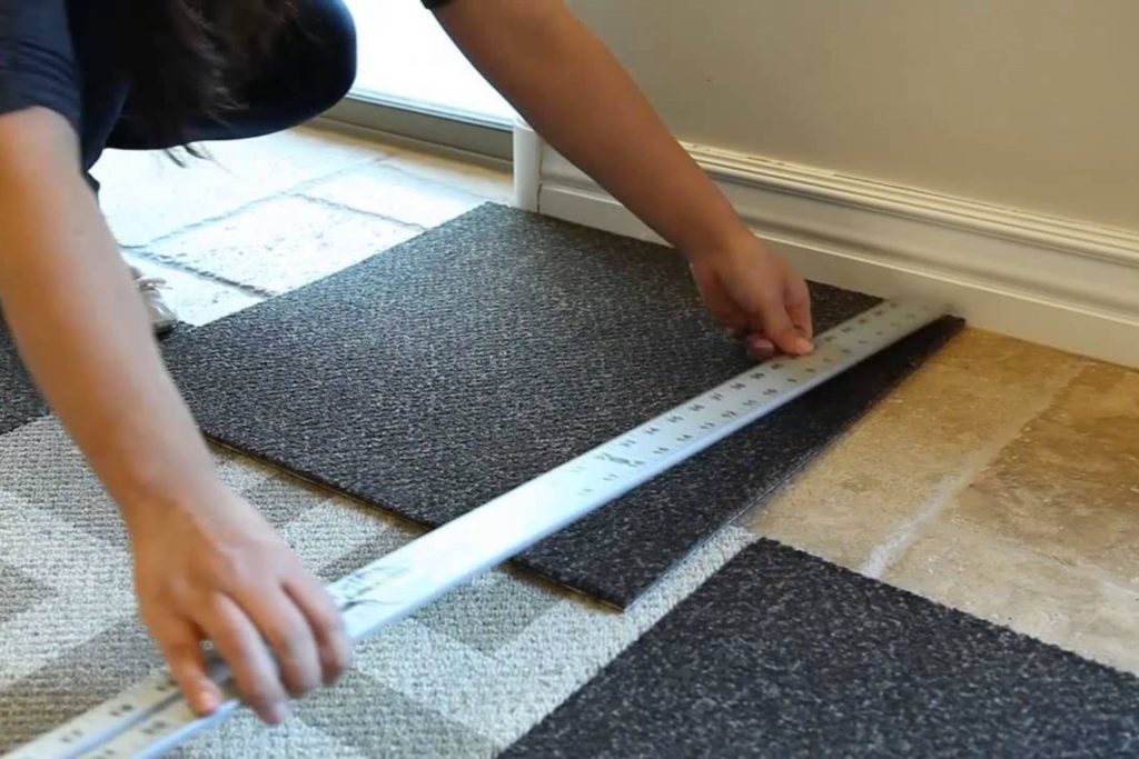 A woman uses a ruler to measure the floor, indicating a carpet tile flooring service in Los Angeles, CA.