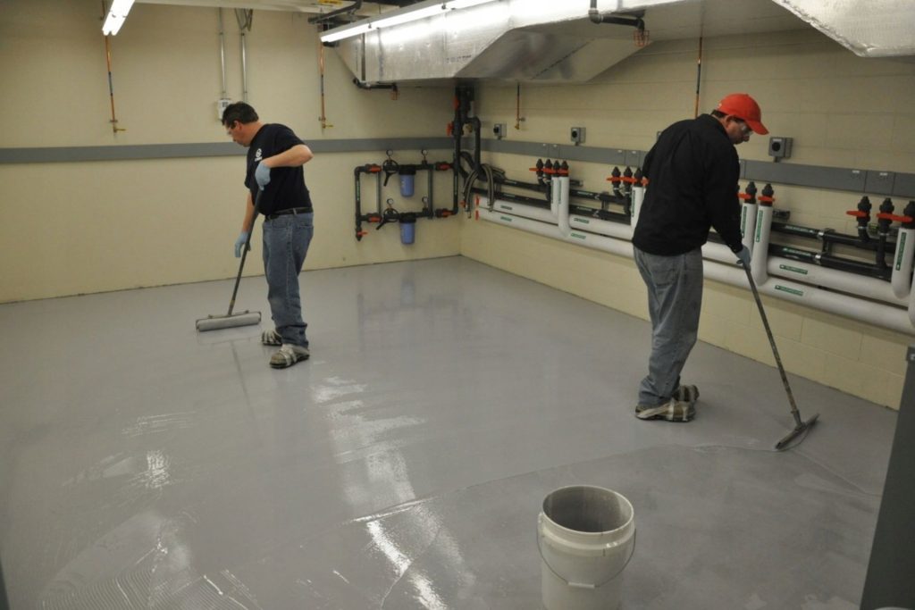 Two men engaged in cleaning a room with a gray floor, showcasing epoxy flooring in Los Angeles, CA.