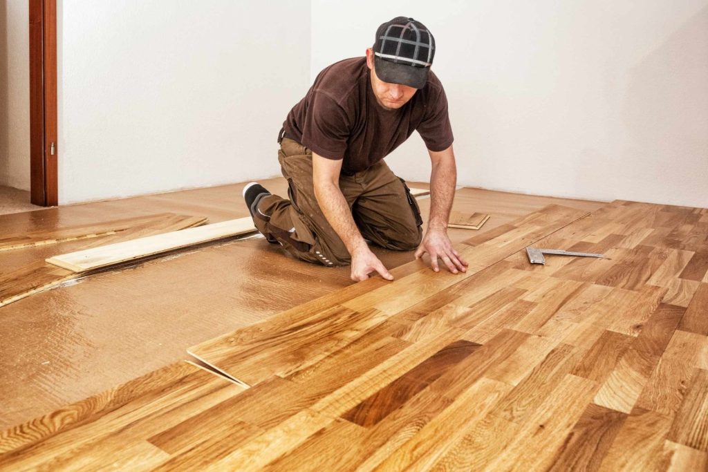 A man is installing wood flooring in a room, highlighting a hardwood flooring service in Los Angeles, CA.