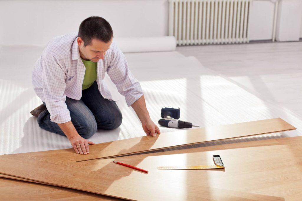 A man laying laminate wood flooring in a room, representing a flooring service based in Los Angeles, CA.