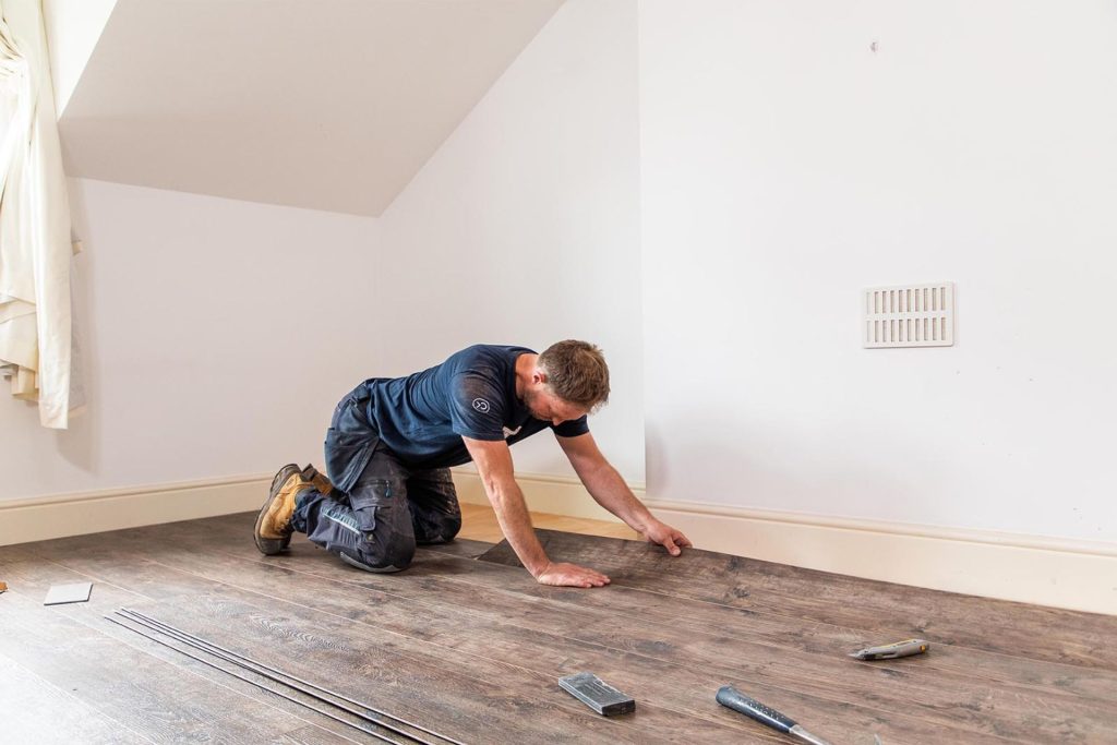 A man is installing luxury vinyl tile flooring in an empty room, representing flooring services in Los Angeles, CA.