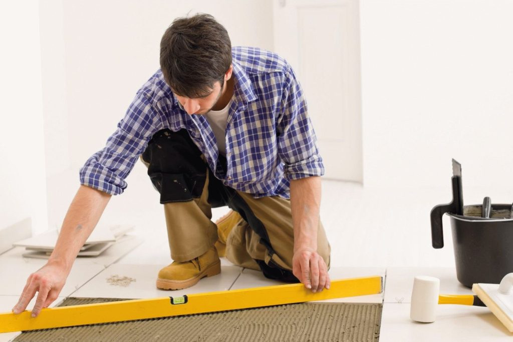 A man uses a measuring tape on the floor, providing tile flooring services in Los Angeles, CA.