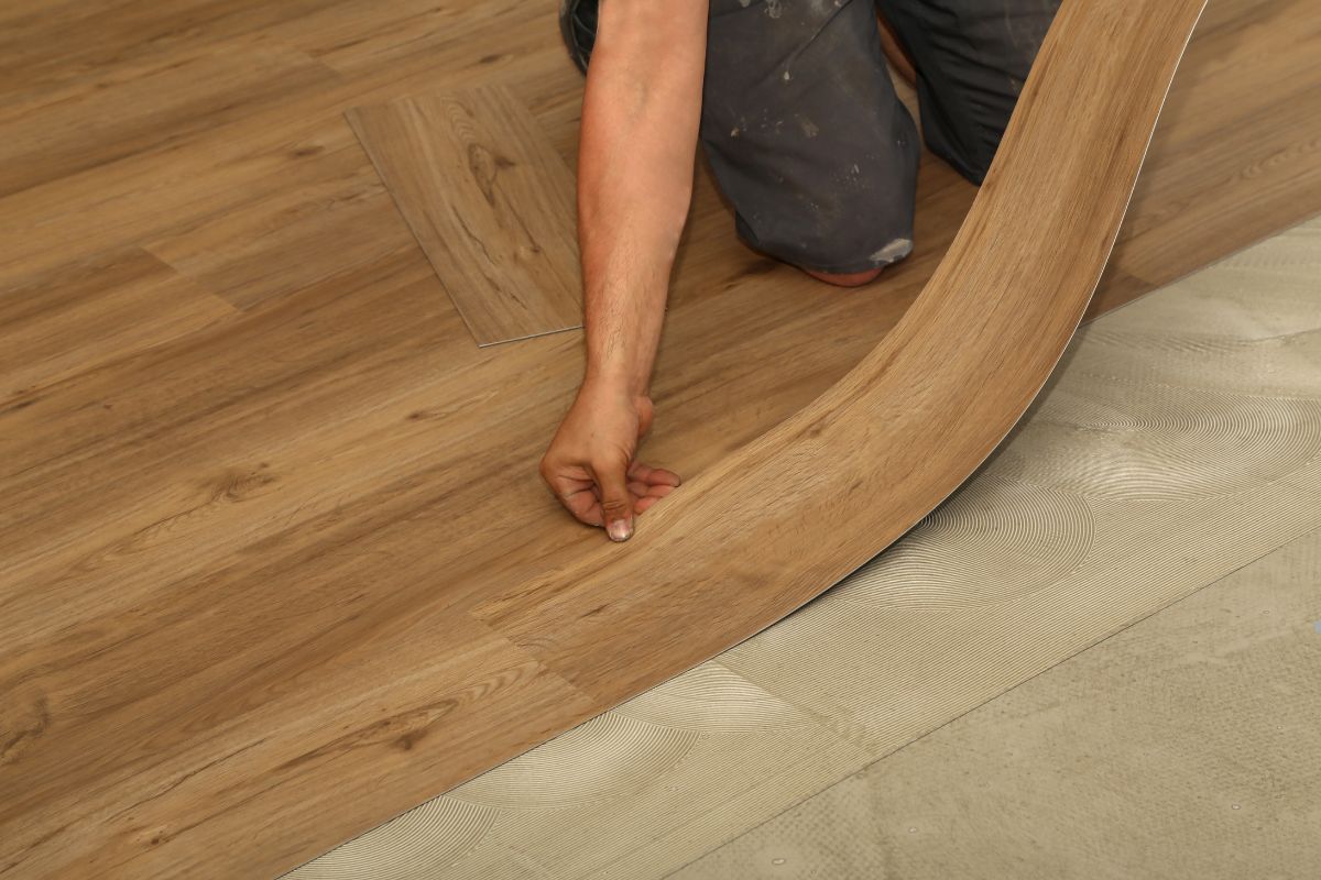 A person installing vinyl flooring by laying down wooden planks in a home renovation project.