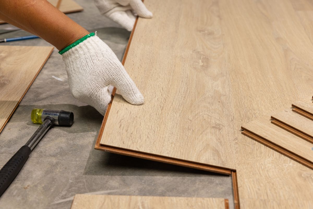A person installing vinyl flooring, carefully laying down planks in a home renovation project.